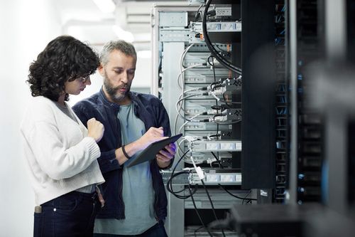 Two technicians working on a tablet in a server room.
